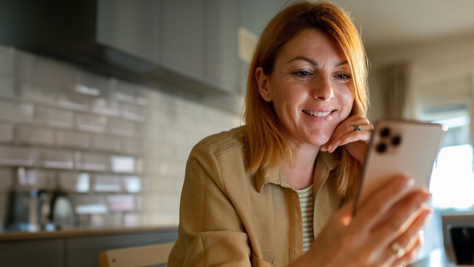 Women standing in a Kitchen smiling while looking at the phone she is holding in her hand